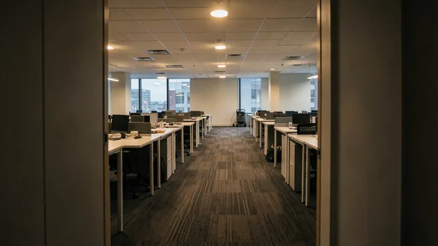 Empty open-plan office floor at dusk with a cleaning trolley parked near the far wall
